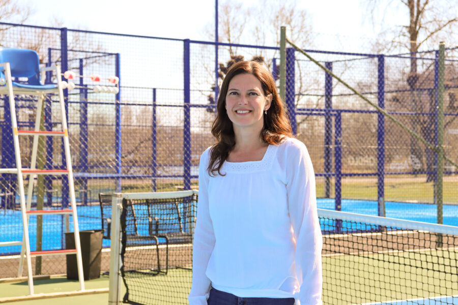 Daniela ler stort mot kameran. Hon står utomhus på padelbanan i Växjö.
